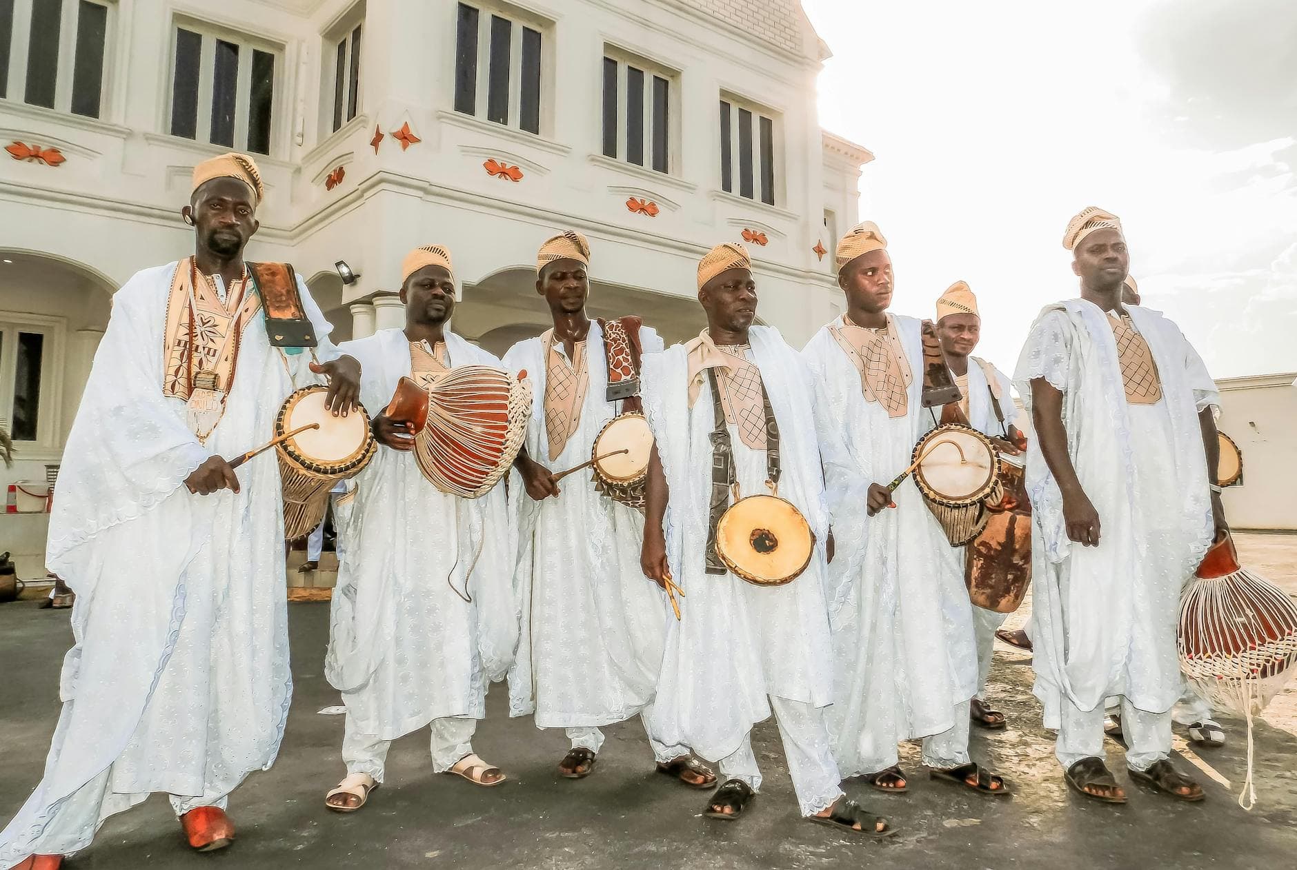 Group of African men in traditional attire with drums in front of a building in Nigeria.
